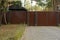 Long metal brown fence and gate at the sidewalk and grass outside