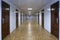 Long office hallway with many doors of dark red wood.