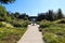 A long paved footpath with a fountain in the center with lush green trees along the path a pink and yellow roses