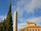 Long pedestal with cross next to a church and cypress tree