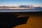 Long, pointy shadows cast by wooden beach huts on sand at sunset