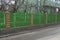 Long private fence of green wooden planks and brown bricks