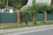 A long private wall of a fence made of brown bricks and green metal