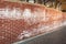 A long red brick wall stained with white efflorescence, a crystalline of salt, formed due to water being present