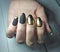 Long round nails with black matte gel polish and gold design. Manicure on women`s hands with gel coating.