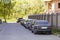 Long row of cars parked in quiet neighborhood on clean empty paved street along new stone fence on background of unfinished brick