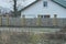 Long rural fence made of wooden boards and bricks in front of an honest white house