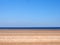 Long sandy beach with blue summer sky and blue sea with a group distant unidentifiable people near the water