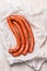 Long sausage meat in white wrapping paper on wooden background, top view