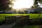 Long shadows fallen over wooden bridge as sunset beams through the folliage behind