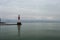 Long shot of light tower peaking out from side of frame with calm lake and intense cloudy sky