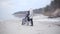 Long shot of thoughtful Caucasian woman standing with disabled son in wheelchair on sandy river bank. Portrait of mother