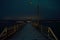 Long snowy wooden pier with faint aurora borealis over mountain and fjord