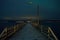 Long snowy wooden pier with faint aurora borealis over mountain and fjord