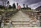 Long stairs leading up to an old rose colored church under an expressive overcast sky