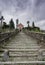 Long stairs leading up to an old rose colored church under an expressive overcast sky