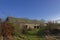 A long Stone built barn with a pitched slate roof, abandoned and set within the overgrown grounds of a Farmhouse