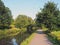 A long straight path along a canal in summer with trees reflected in the water in bright summer sunlight near luddenden