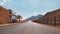 Long straight road with desert hills in distance, brick wall and iron fence on sides. Scenery at the entrance to Wadi