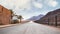 Long straight road with desert hills in distance, brick wall and iron fence on sides. Scenery at the entrance to Wadi Rum