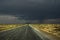 Long straight road to the horizon somewhere in Utah with a rain storm passing through in the distance