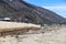 A long stretch of a concrete bridge at beach with RVs parked along the street and rocks along the beach with silky sand