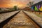 A long stretch of metal and wooden railroad tracks surrounded by gravel, red brick buildings and lush green trees