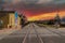 A long stretch of railroad tracks covered in gravel with a black metal fence and buildings along the tracks and blue sky