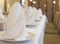 Long table in a restaurant covered with white tablecloth and served with white plates and napkins