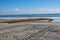 Long thick rusty pipe running along wet beach sand and entering the ground at the edge of the ocean