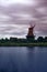 Long time exposure of windmill behind pond against cloudy sky with gloomy atmosphere