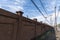 Long view down a sidewalk bordered by a street and a tall stucco wall topped with barbed wire, blue sky with clouds industrial lan