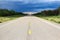 The long view of a highway with a storm brewing in the distance