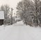 Long village road covered with snow, snow on trees, houses in the village, power pole in winter