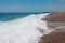 Long waves along rocky beach with pier in the distance