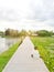 A long white wooden pathway past a pond at the end of the path with people sitting beneath the dark clouds