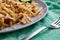 Long and wide pasta spaghetti noodles under viscous melted cheese on a platter with sliced â€‹â€‹fresh cucumbers on a bright green