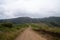 Long, winding hiking trail leading to mountains with two hikers marching into distance