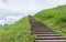 Long wood stairs to top of grass-covered earth-deposit