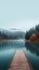 Long wooden dock on a misty serene lake in autumn. Fall landscape with mountains and trees. Pier on a calm pond.