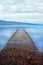 A long wooden jetty on a lake, looking out over a straight out over a clear calm blue lake