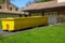 A long yellow empty dumpster seen in the driveway in front of a home being renovated