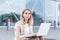 Longing young woman sitting alone on street sidewalk on urban background modern building. Sad girl Student or businesswoman misses