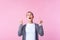 Look above! Portrait of amazed brunette teen girl standing with open mouth in surprise, pointing up at copy space. pink background