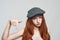 Look here Portrait of young rude redhead woman in headgear looking at camera and gesturing while standing against grey