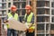 Look here Two young builders in working uniform and helmets are holding a construction drawing in their hands and