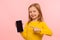 Look at my cellphone! Adorable glad little girl pointing smartphone and smiling at camera, advertising of mobile device