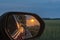 Look in the outside mirror of a moving car. In the mirror you can see the setting sun, parts of the vehicle and a bicycle