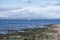 Looking across moss covered rocks over to a loan fishing boat and in the far distance wind turbines above Ardrossan