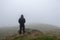 Looking at the back of a hooded figure looking out on a foggy , moody day. On a bleak hillside in winter. With copy space.